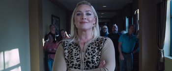 Movie still from “Notorious Nick” (2021), directed by Aaron Leong – A woman standing in front of a group of people in a room; Close Up shot, Low angle