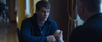 Movie still from “Notorious Nick” (2021), directed by Aaron Leong – A young man holding an object while sitting down; Close Up shot, Over the shoulder angle