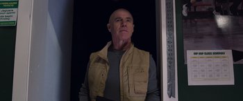 Movie still from “Notorious Nick” (2021), directed by Aaron Leong – A man with a bald head wearing a tan vest; Medium shot, Low angle