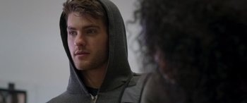 Movie still from “Notorious Nick” (2021), directed by Aaron Leong – A young man wearing a gray hoodie is talking to a woman; Close Up shot, Over the shoulder angle