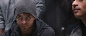Movie still from “Notorious Nick” (2021), directed by Aaron Leong – A young man wearing a gray hat and a gray jacket; Close Up shot, Over the shoulder angle