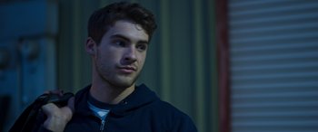 Movie still from “Notorious Nick” (2021), directed by Aaron Leong – A young man in a black hoodie looking to his left; Close Up shot, Low angle