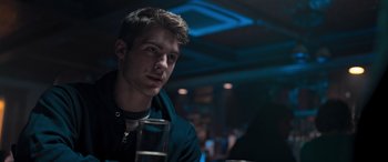 Movie still from “Notorious Nick” (2021), directed by Aaron Leong – A man sitting at a table with a drink in front of him; Close Up shot, Over the shoulder angle