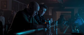 Movie still from “Notorious Nick” (2021), directed by Aaron Leong – A couple of men sitting at a table with a drink; Medium shot, Over the shoulder angle