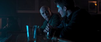 Movie still from “Notorious Nick” (2021), directed by Aaron Leong – Two men sitting at a table with a drink; Medium shot, Over the shoulder angle