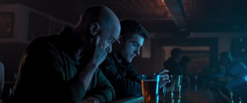 Movie still from “Notorious Nick” (2021), directed by Aaron Leong – Two men sitting at a bar with a beer; Medium shot, Over the shoulder angle