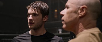 Movie still from “Notorious Nick” (2021), directed by Aaron Leong – A man standing next to another man in front of a building; Close Up shot, Over the shoulder angle