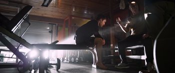 Movie still from “Notorious Nick” (2021), directed by Aaron Leong – A man sitting on top of a bench in a gym; Wide shot, Low angle