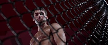 Movie still from “Notorious Nick” (2021), directed by Aaron Leong – A shirtless man standing in front of a chain link fence; Close Up shot, Low angle