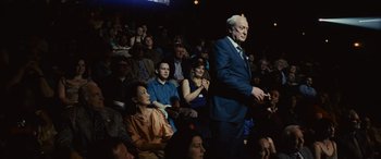 Movie still from “Now You See Me” (2013), directed by Louis Leterrier – A man in a blue suit stands in front of an audience; Medium shot, Over the shoulder angle