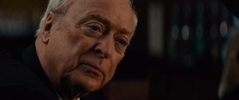 Movie still from “Now You See Me” (2013), directed by Louis Leterrier – An older man looking at the camera while wearing glasses; Close Up shot, Over the shoulder angle