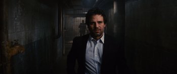 Movie still from “Now You See Me” (2013), directed by Louis Leterrier – A man wearing a suit and tie standing in a dark room; Medium shot, Over the shoulder angle