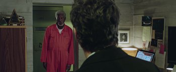 Movie still from “Now You See Me 2” (2016), directed by Jon M. Chu – An older man in a red jumpsuit looking in the mirror; Medium shot, Over the shoulder angle