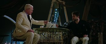 Movie still from “Now You See Me 2” (2016), directed by Jon M. Chu – Two men are sitting at a table and one of them is holding a cup; Medium shot, Over the shoulder angle