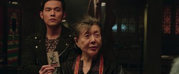 An older woman is looking at the camera while a younger man looks on