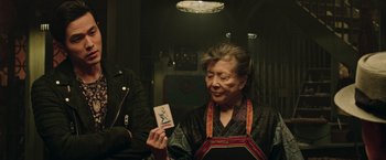 Movie still from “Now You See Me 2” (2016), directed by Jon M. Chu – An older woman holding up an item in her hand; Medium shot, Over the shoulder angle