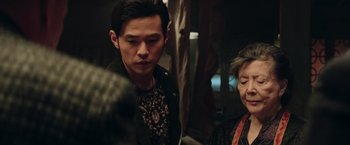 Movie still from “Now You See Me 2” (2016), directed by Jon M. Chu – A man standing next to an older woman in a room; Close Up shot, Over the shoulder angle