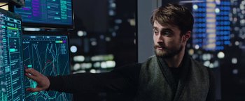 A man with a goatee is looking out a window at night