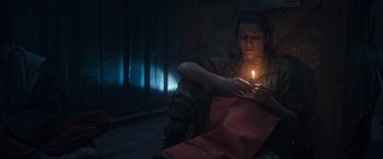 Movie still from “Nowhere” (2023), directed by Albert Pintó – A person sitting on the ground with a candle in their hand; Medium shot, Low angle