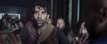 Movie still from “Nowhere” (2023), directed by Albert Pintó – A group of people in a room with a man in the foreground looking at the camera; Close Up shot, Over the shoulder angle