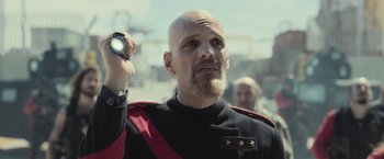 Movie still from “Nowhere” (2023), directed by Albert Pintó – A bald man in a black and red uniform holding a flashlight; Close Up shot, Over the shoulder angle