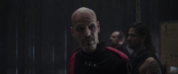 Movie still from “Nowhere” (2023), directed by Albert Pintó – A man with a bald head wearing a black and red uniform; Close Up shot, Low angle