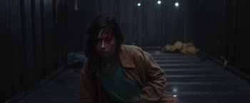 Movie still from “Nowhere” (2023), directed by Albert Pintó – A woman with a bruised face sitting on steps in the dark; Medium shot, High angle