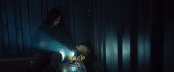 Movie still from “Nowhere” (2023), directed by Albert Pintó – A person sitting in a dark room with a flashlight; Medium shot, High angle