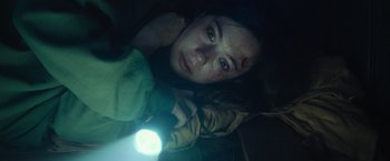 Movie still from “Nowhere” (2023), directed by Albert Pintó – A young woman is laying in the dark with a flashlight; Close Up shot, High angle