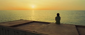 Movie still from “Nowhere” (2023), directed by Albert Pintó – A woman sitting on the edge of a pier looking out at the ocean; Extreme Wide shot, High angle