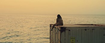 Movie still from “Nowhere” (2023), directed by Albert Pintó – A woman sitting on a dock looking out at the ocean; Extreme Wide shot, High angle