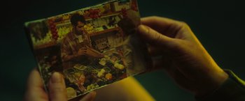 Movie still from “Nowhere” (2023), directed by Albert Pintó – A person holding up a picture of a person in a kitchen; Extreme Close Up shot, Overhead angle