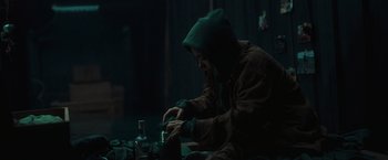 Movie still from “Nowhere” (2023), directed by Albert Pintó – A person sitting in a dark room with a bottle of alcohol; Medium shot, High angle