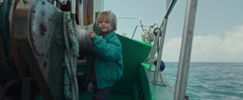 Movie still from “Nowhere” (2023), directed by Albert Pintó – A little boy standing on the side of a green boat; Medium shot, Low angle