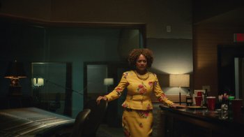 Movie still from “Atlanta” (2016), created by Donald Glover – A woman in a yellow suit standing in front of a desk; Medium shot, Low angle