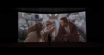 Movie still from “Obi-Wan Kenobi: A Jedi's Return” (2022), directed by David Gelb – A man standing in front of a large screen with star wars characters; Wide shot, Over the shoulder angle