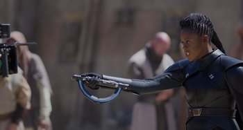 Movie still from “Obi-Wan Kenobi: A Jedi's Return” (2022), directed by David Gelb – A man in a black and blue outfit holding a metal object; Medium shot, Over the shoulder angle
