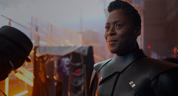 Movie still from “Obi-Wan Kenobi: A Jedi's Return” (2022), directed by David Gelb – A woman in a black outfit standing in front of a building; Close Up shot, Over the shoulder angle