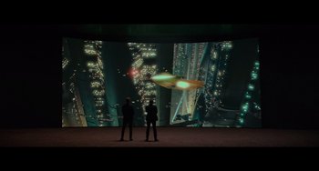 Movie still from “Obi-Wan Kenobi: A Jedi's Return” (2022), directed by David Gelb – Two people standing in front of a projection of a city at night; Extreme Wide shot, Low angle