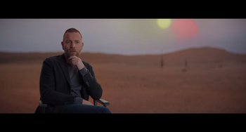 Movie still from “Obi-Wan Kenobi: A Jedi's Return” (2022), directed by David Gelb – A man sitting in a chair in the middle of the desert; Medium shot, Over the shoulder angle