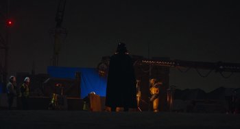 Movie still from “Obi-Wan Kenobi: A Jedi's Return” (2022), directed by David Gelb – A darth vader standing in front of a construction site at night; Wide shot, Over the shoulder angle