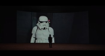 Movie still from “Obi-Wan Kenobi: A Jedi's Return” (2022), directed by David Gelb – A man standing in front of a large star wars figure projected on a wall; Wide shot, Low angle