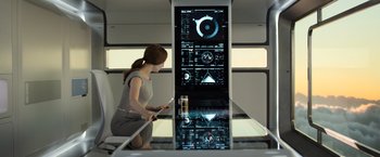 Movie still from “Oblivion” (2013), directed by Joseph Kosinski – A woman in a gray dress is looking at a screen; Medium shot, Over the shoulder angle