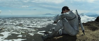 Movie still from “Oblivion” (2013), directed by Joseph Kosinski – A man sitting on the beach with a cup of water; Wide shot, Low angle