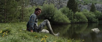 Movie still from “Oblivion” (2013), directed by Joseph Kosinski – A man sitting on the grass next to a body of water; Medium shot, Low angle