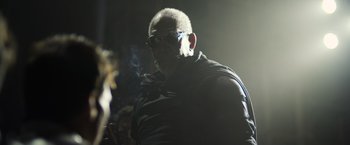 Movie still from “Oblivion” (2013), directed by Joseph Kosinski – A man with sunglasses smoking a cigarette in a dark room; Close Up shot, Low angle