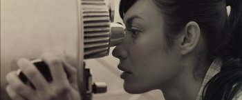 Movie still from “Oblivion” (2013), directed by Joseph Kosinski – A woman looking into a projector while wearing a black and white photo; Close Up shot, High angle