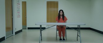 Movie still from “Ocean's Eight” (2018), directed by Gary Ross – A person sitting at a table in an empty room; Wide shot, High angle