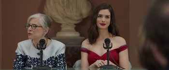 Movie still from “Ocean's Eight” (2018), directed by Gary Ross – Two women are sitting at a table with a microphone; Close Up shot, Low angle