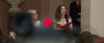 Movie still from “Ocean's Eight” (2018), directed by Gary Ross – A woman in a red dress speaking into a microphone; Medium shot, Over the shoulder angle